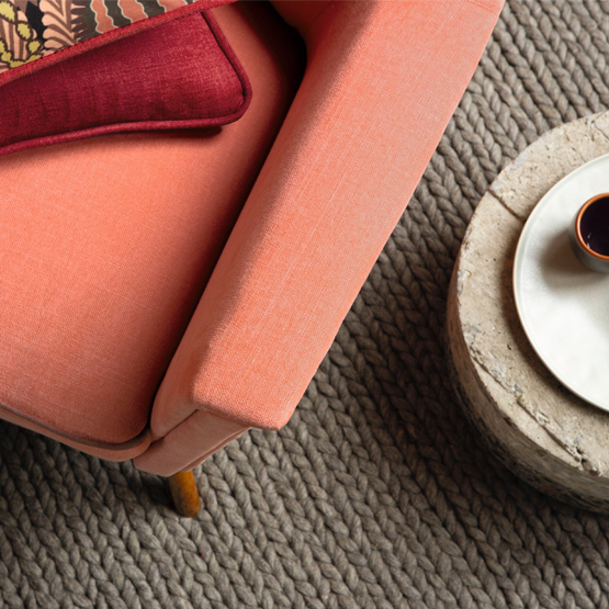 grauer grob geflochtener Teppich mit lachsfarbener Couch